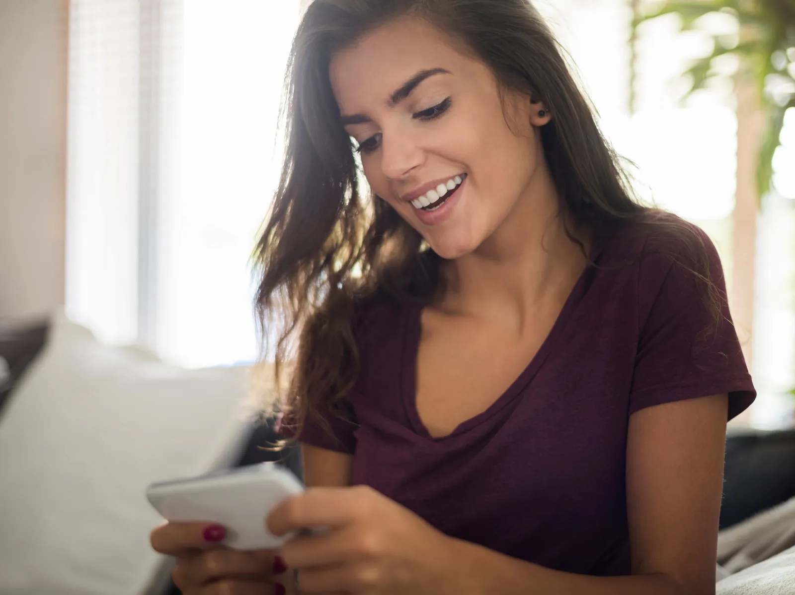 Mulher sorrindo no sofá enquanto usa o celular