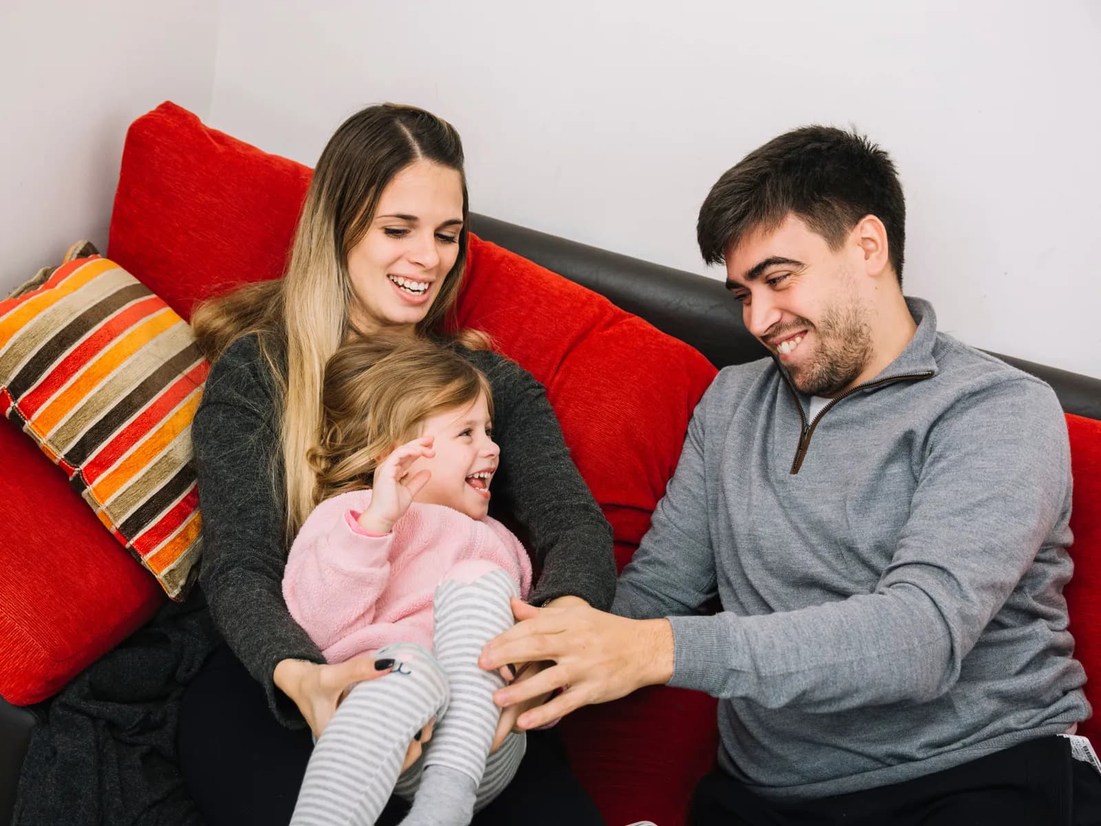 Casal rindo no sofá com a filha pequena